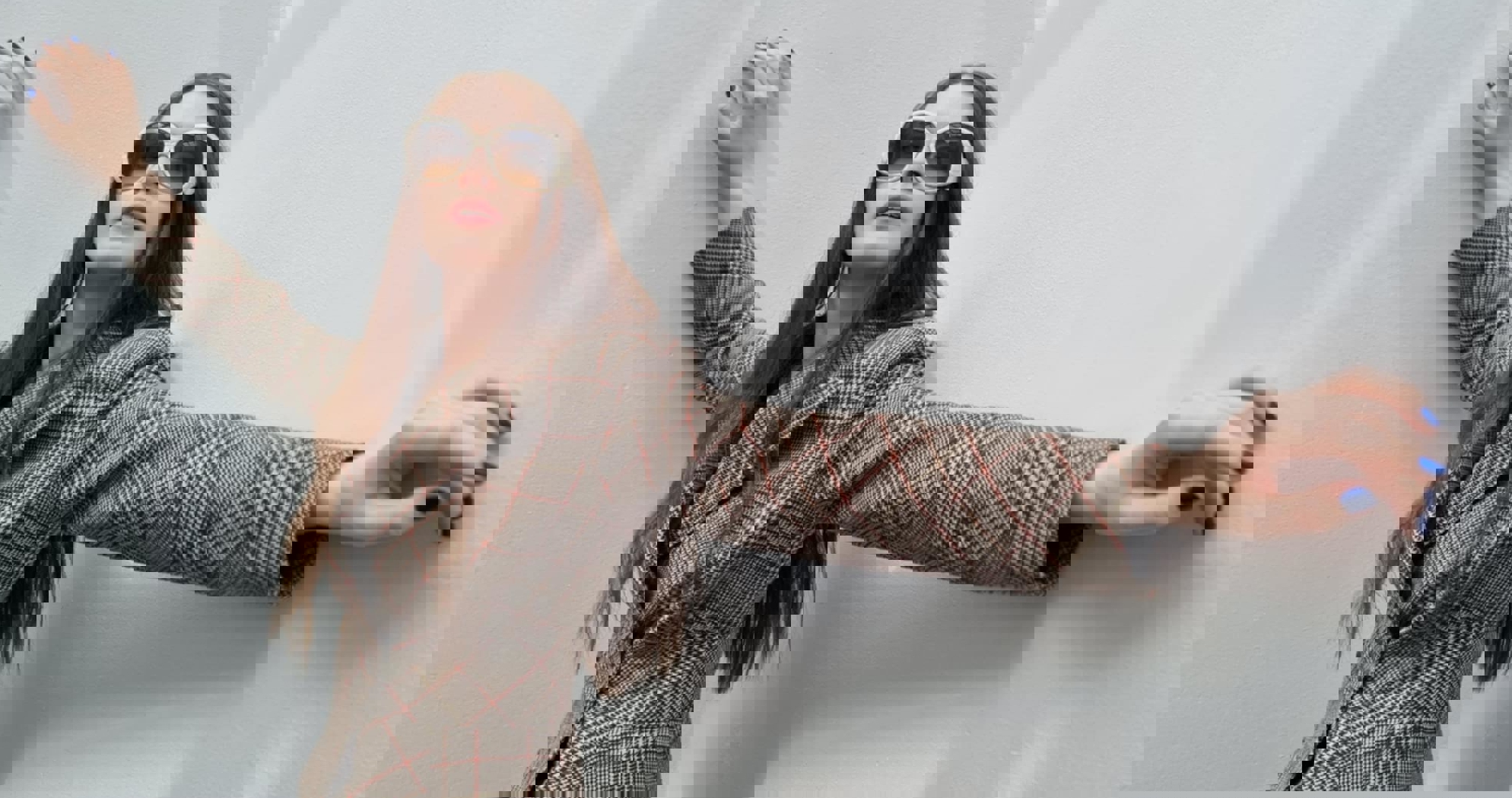 Dame som strekker ut ermene, i brun blazer og solbriller.