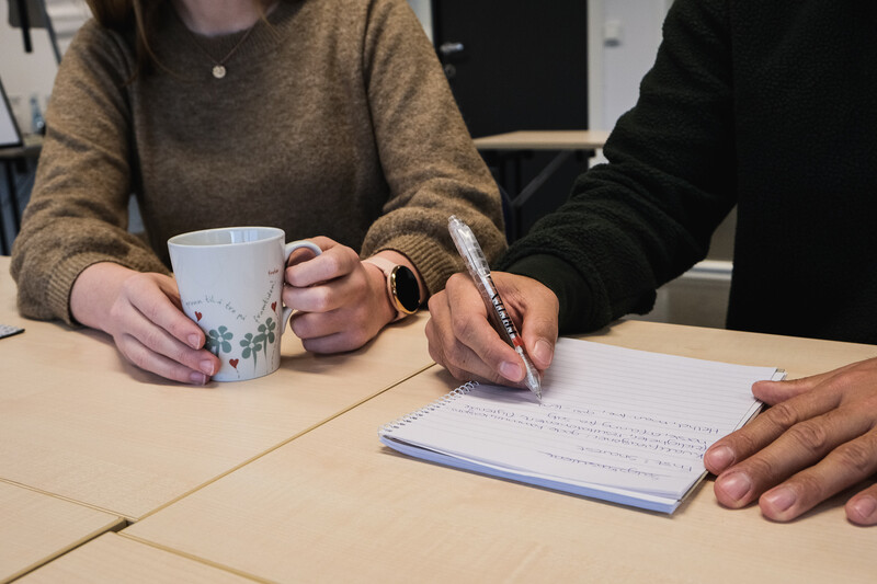 To som sitter ved et bord og noterer på ark